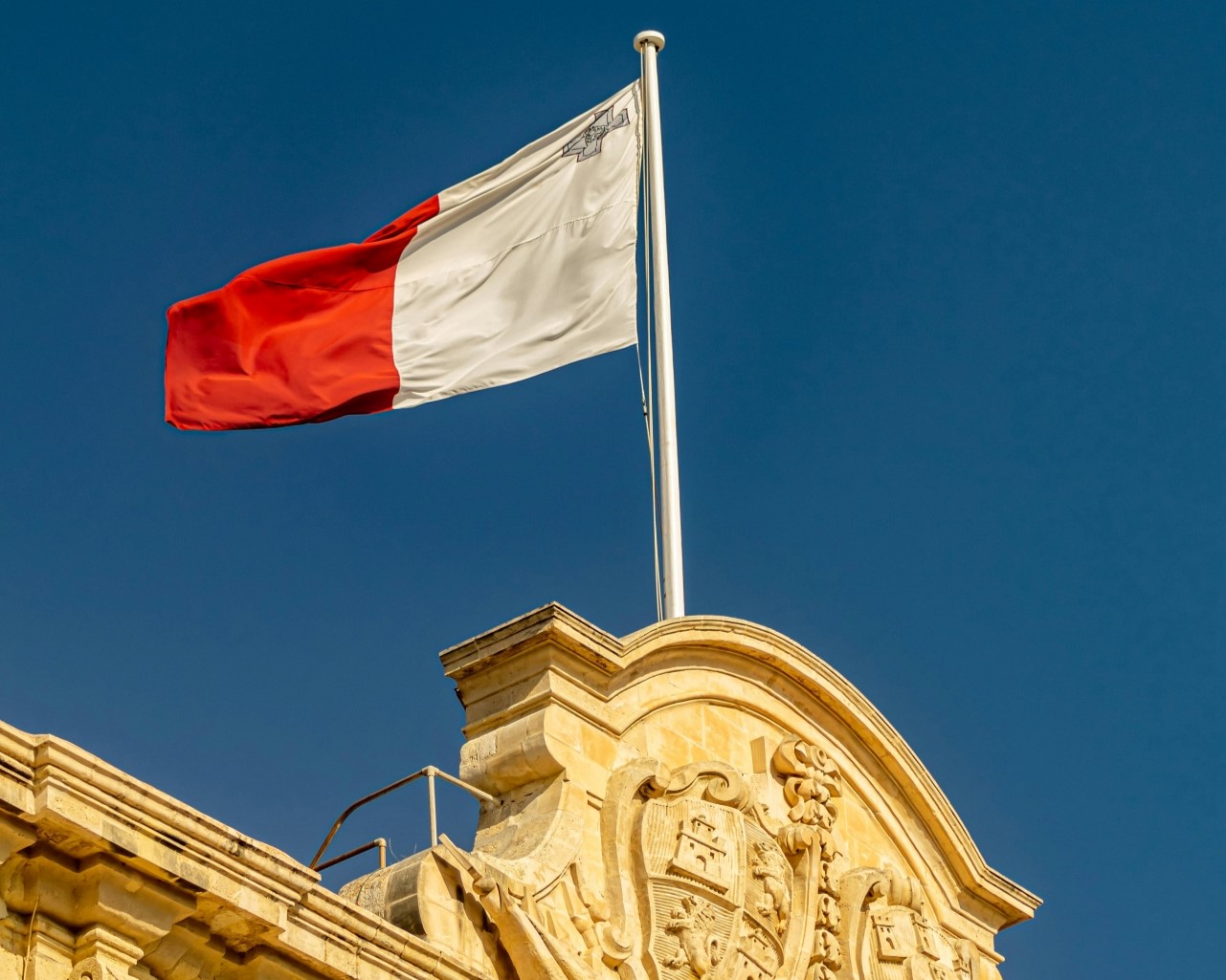 This picture shows a flag of Malta with the white and red colors on top of a stone building.