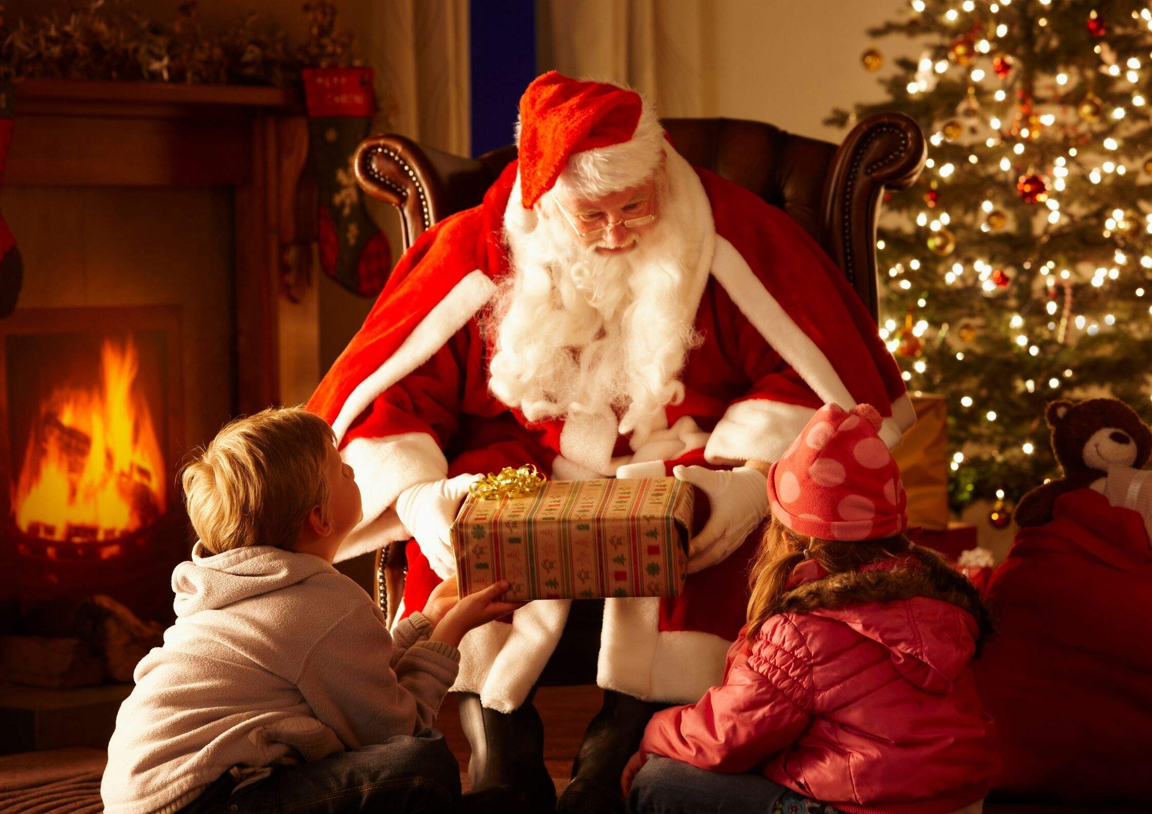 Santa Claus giving children presents by fireplace and Christmas tree. Christmas traditions in Ireland