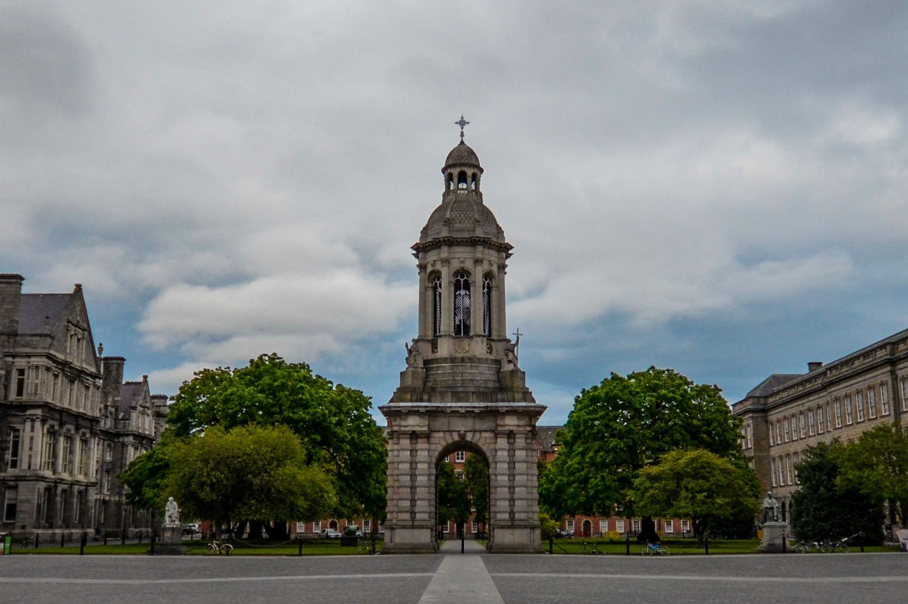 The Campanile bell tower at Trinity College Dublin, surrounded by historic buildings and greenery under a cloudy sky.